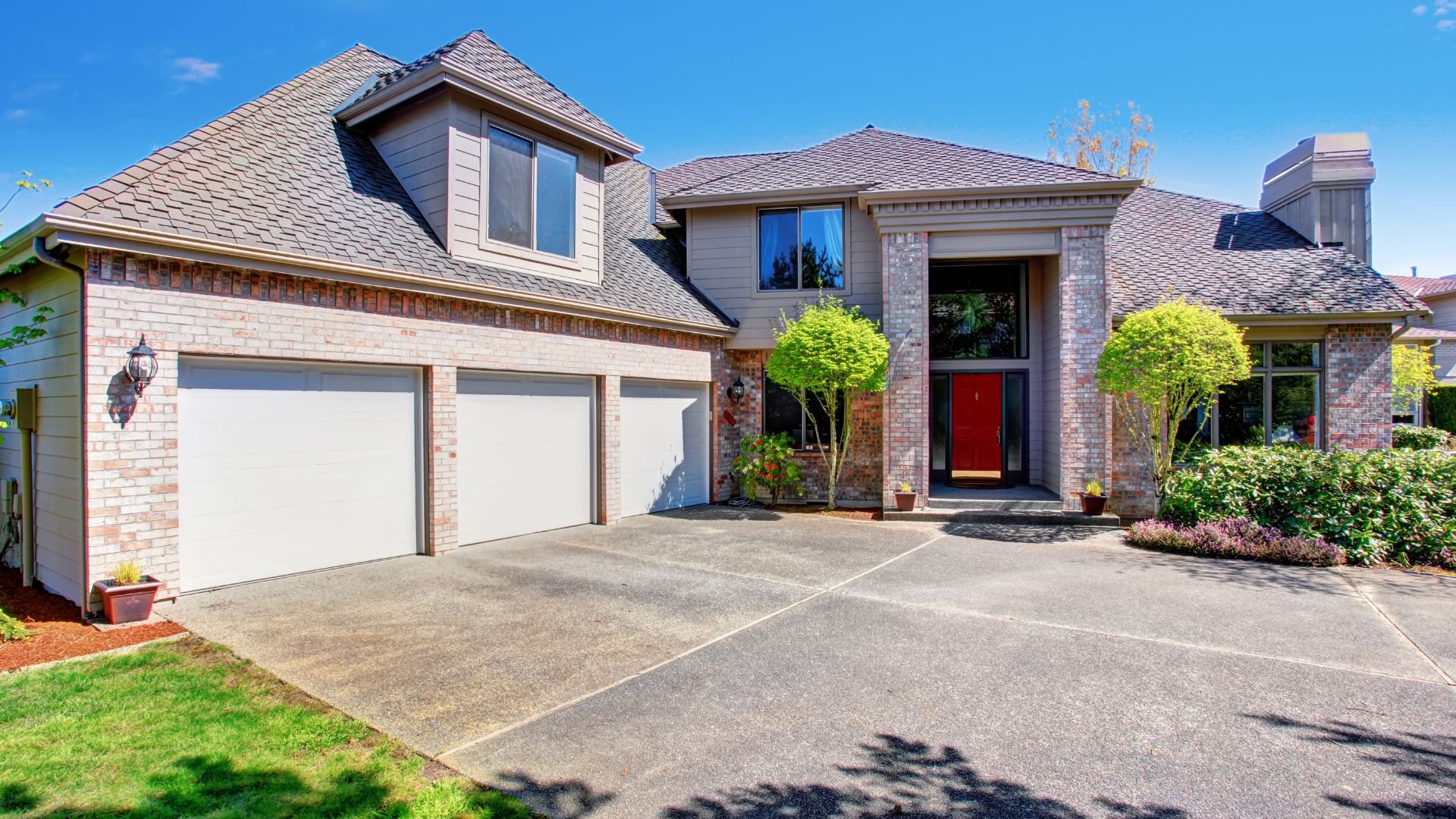 Suburban house with three-car garage, red door, and well-maintained landscaping