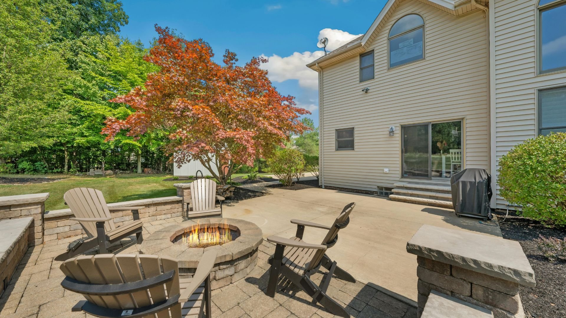 Outdoor patio with fire pit, Adirondack chairs, and colorful autumn tree