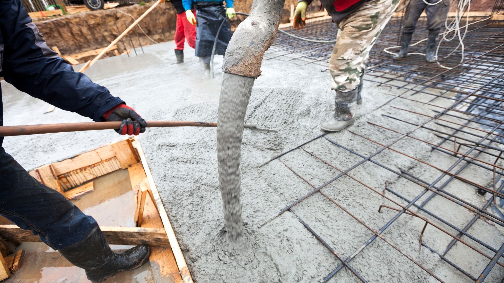Construction workers pouring concrete on reinforced steel mesh foundation
