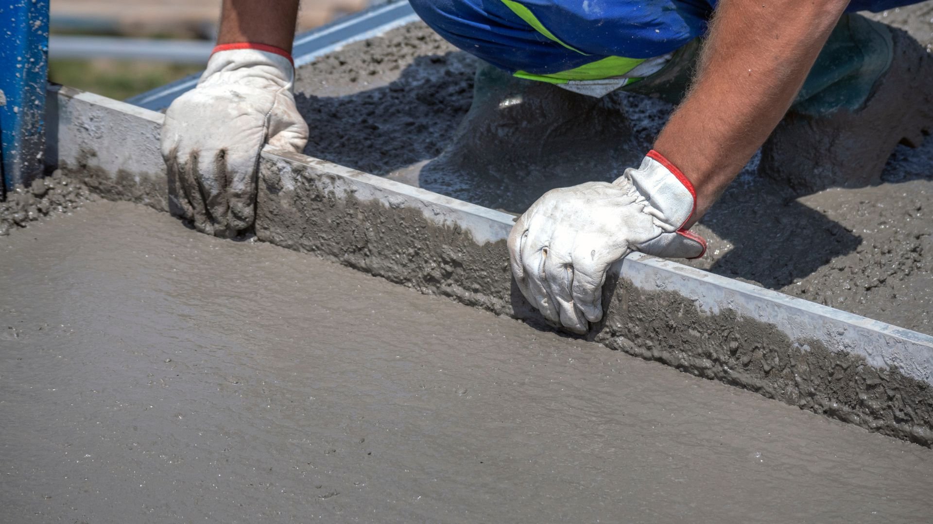 Worker smoothing wet concrete with gloved hands and leveling tool