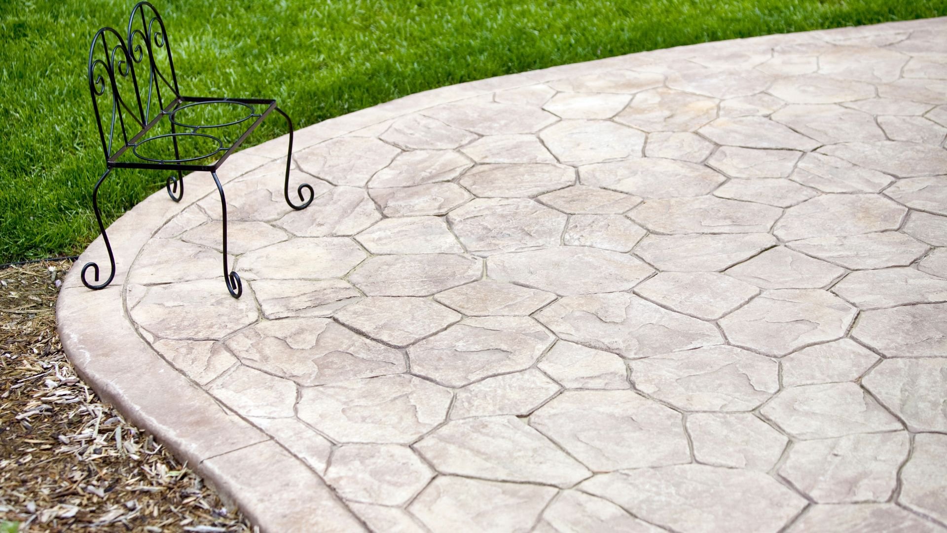 Ornate metal chair on curved stamped concrete patio with green grass