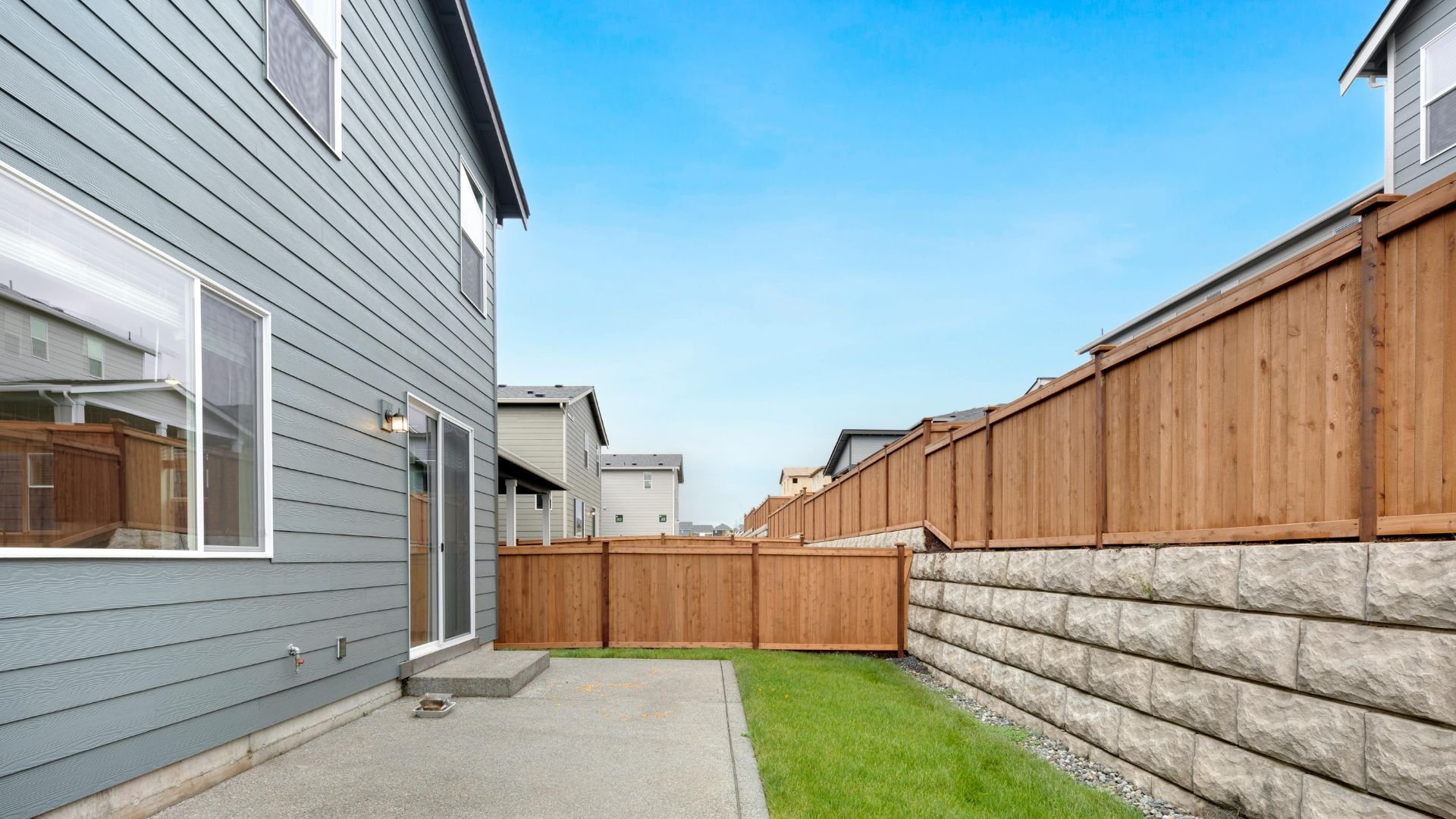 Narrow side yard with concrete patio, wooden fence, and green grass