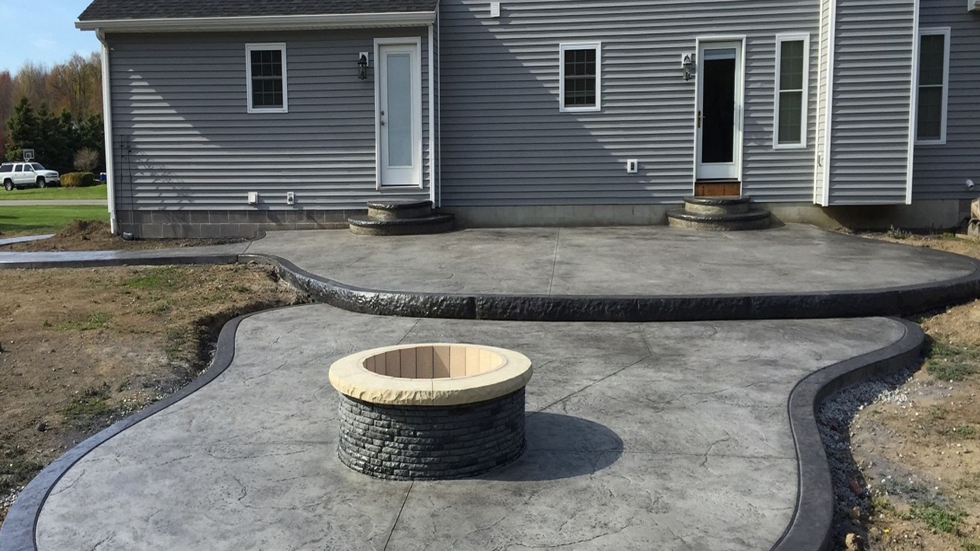 Curved concrete patio with stone fire pit in front of gray house