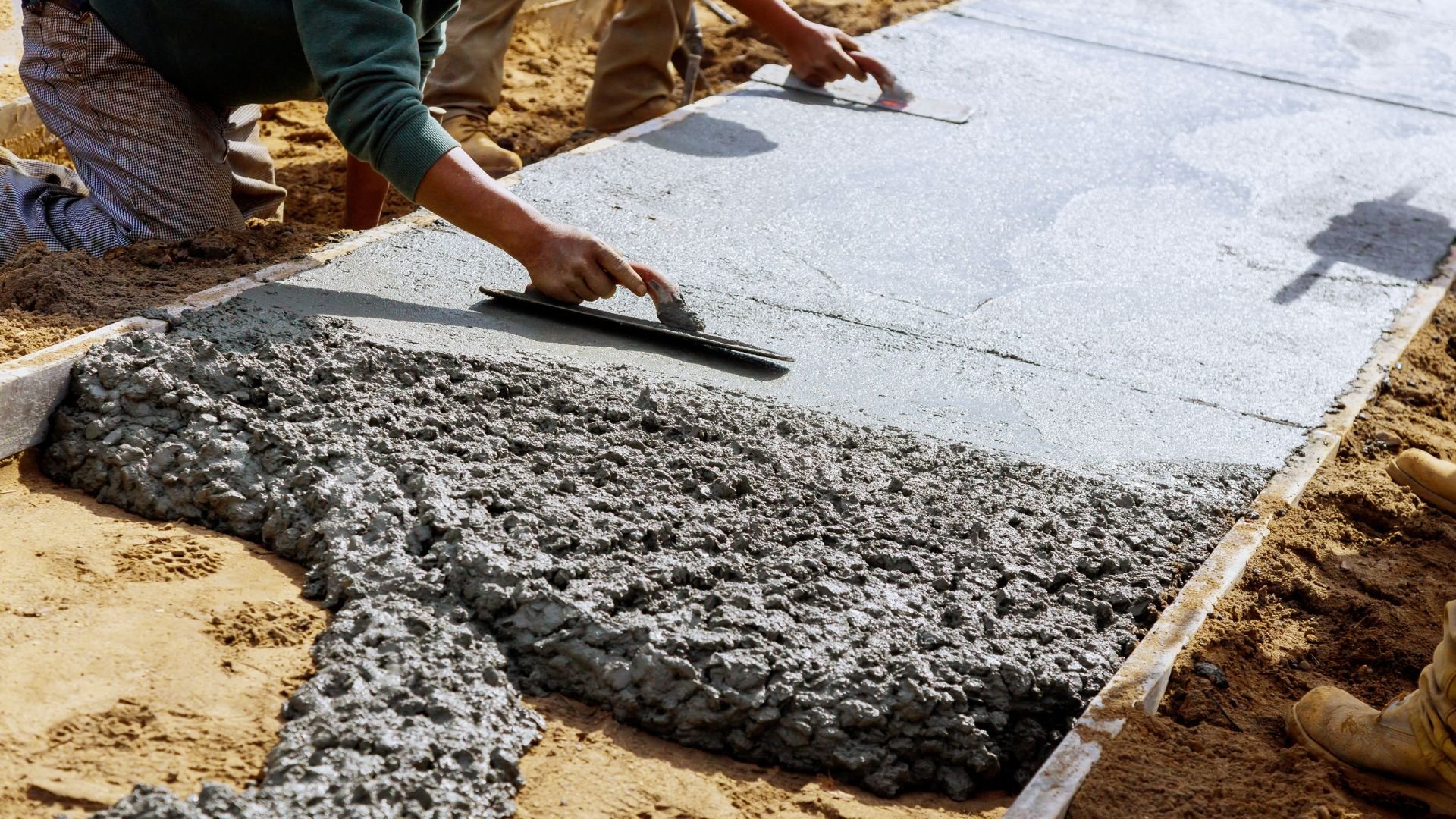 Workers smoothing wet concrete with trowels during sidewalk construction