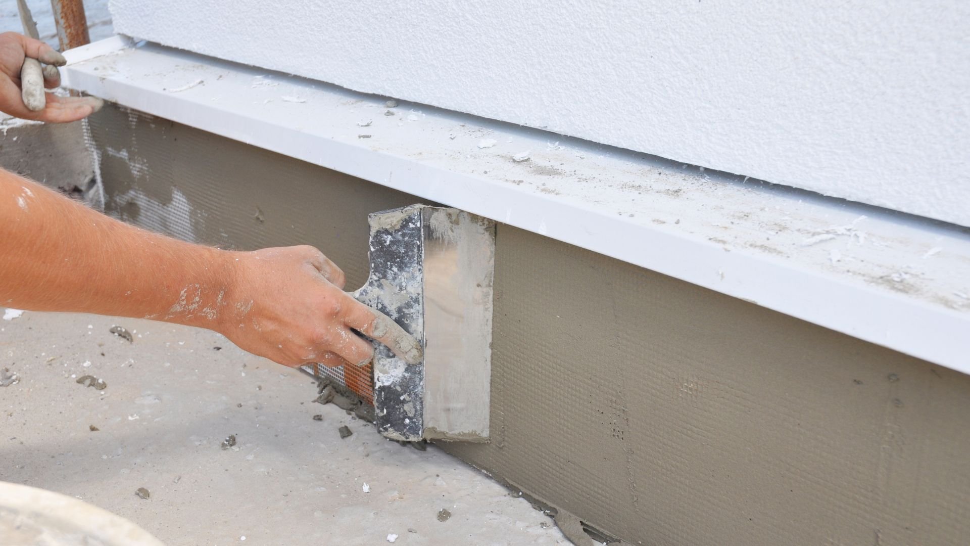 Worker applying cement render to wall with plastering trowel
