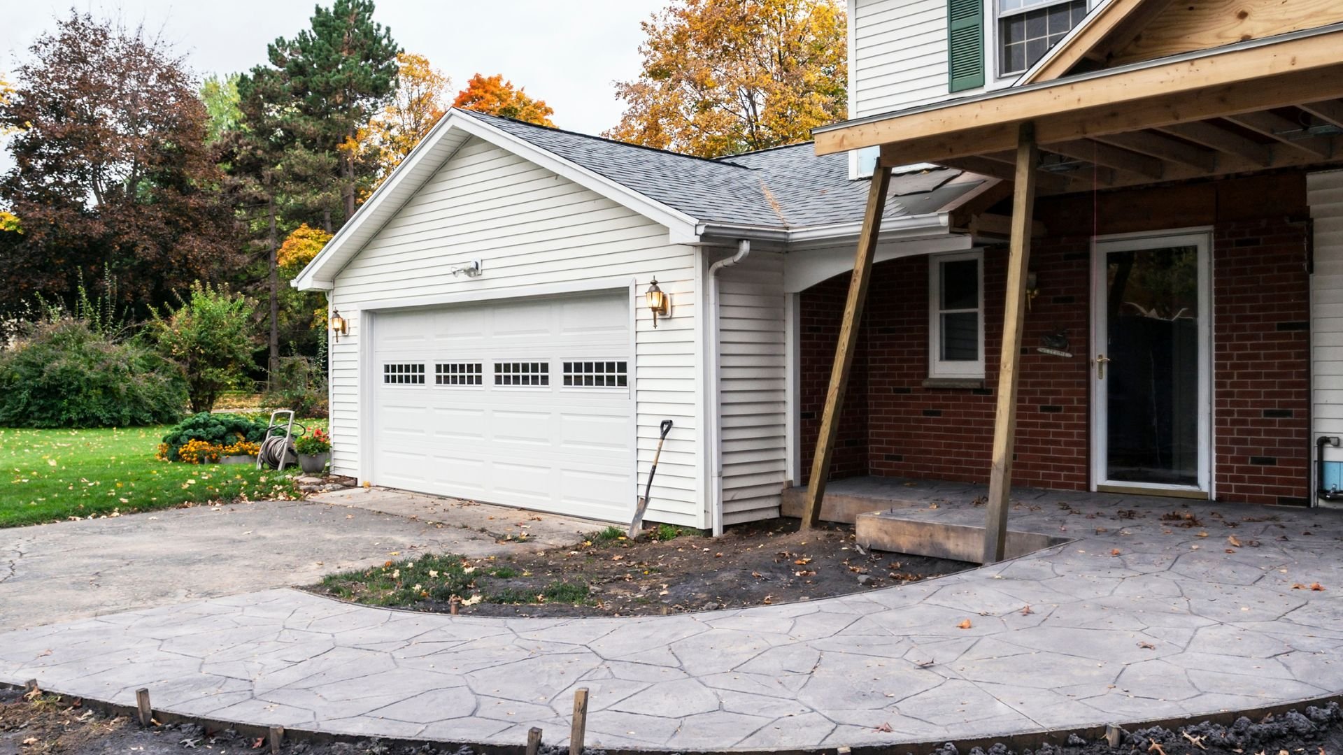 Autumn view of white garage with stone patio and fall trees